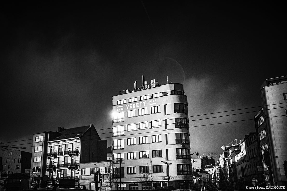 Frontière entre Bruxelles-Ville et Molenbeek, la Porte de Flandre s'ouvre au regard dans un éclat de lumière pour nous montrer un immeuble dominé par l'enseigne de la bière Vedett qui s'intègre au style vintage de la gentrification.© 2014 Bruno D'ALIMONTE