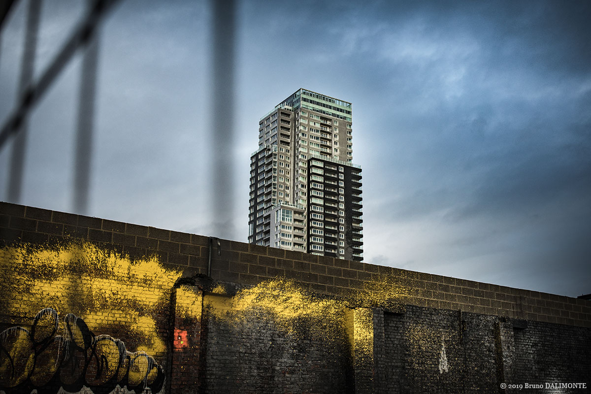 photographie esthétique de la tour bruxelloise UP-Site depuis l'avenue du port avec un mur tagué de couleur jaune intense devant elle. © 2019 Bruno D'Alimonte