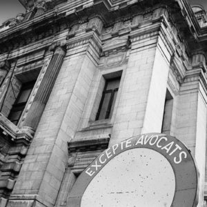 Photographie en noir et blanc du palais de justice de Bruxelles avec comme avant-plan un panneau d