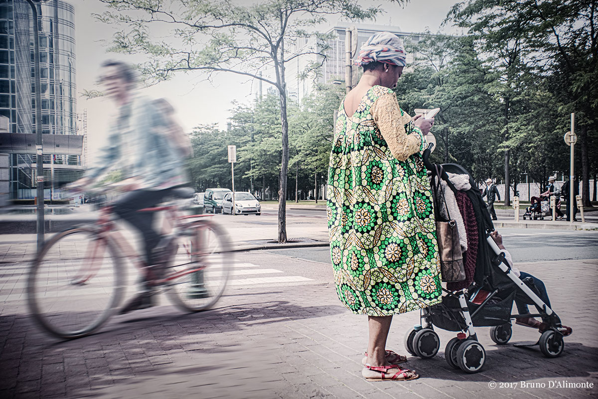 Bruxelles, maman africaine au pagne coloré et poussette tient en ses main un smartphone tandis qu'un cylciste passe dans le quartier Nord et Bolivar © 2017 Bruno D'Alimonte