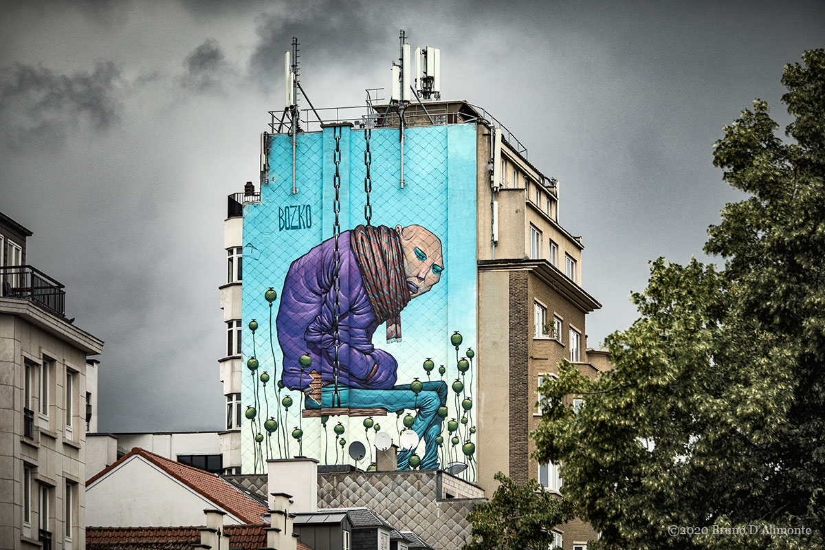 Fresque du "street artist" Bozko située à deux pas de la place Saint Catherine de Bruxelles. Elle représente un personnage au crane rasé assis sur une balançoire qui semble suspendu.