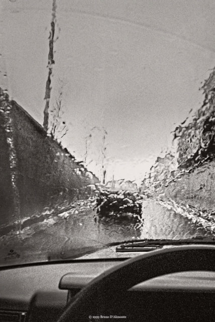 Photographie d'une voiture sous une pluie battante dont l'eau ruisselle depuis le pare-brise à la sortie Simonis de la petite ceinture de Bruxelles au niveau du tunnel Léopold II. © 1999 Bruno D'ALIMONTE