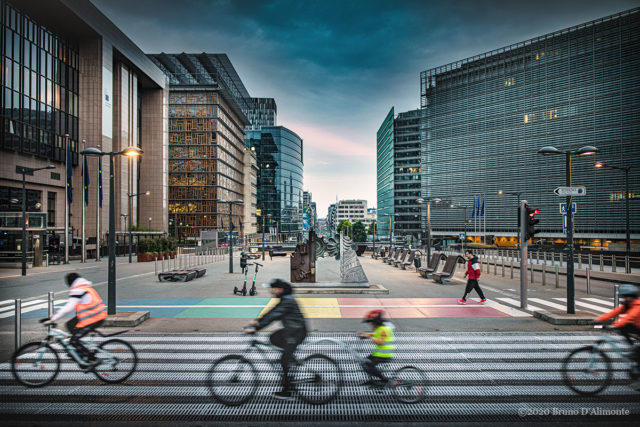 Place Shuman juin 2020, un passage piéton célèbre la cause LGBT tandis que des piétons et des vélos circulent. Illustration de Bruno D'ALIMONTE pour Brussels Eyes