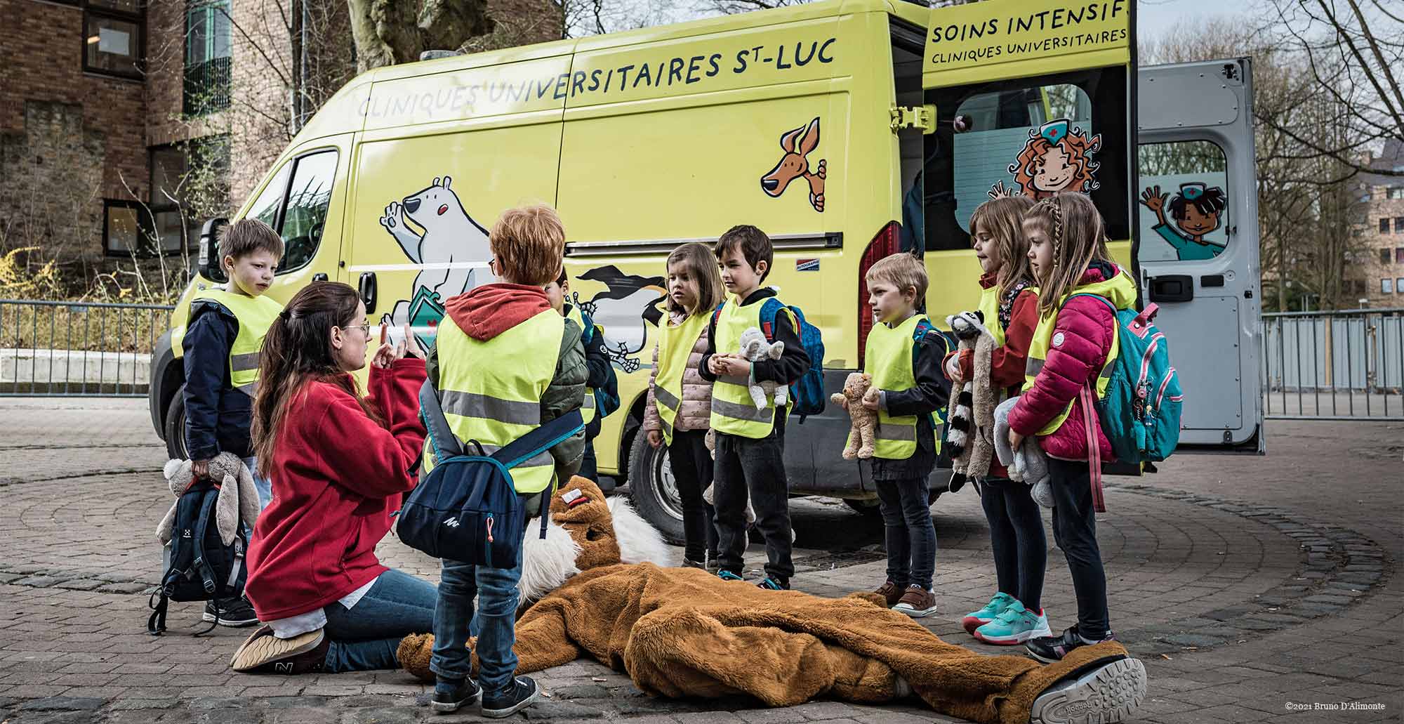 La clinique des nounours à Bruxelles. Des enfants entourent un nounours géant inconscient devant une ambulance ludique
