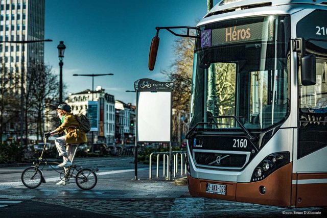 Destination Héros, est une photographie qui représente une cycliste à côté d'un gros bus Stib n38 en destination du square des Héros. 